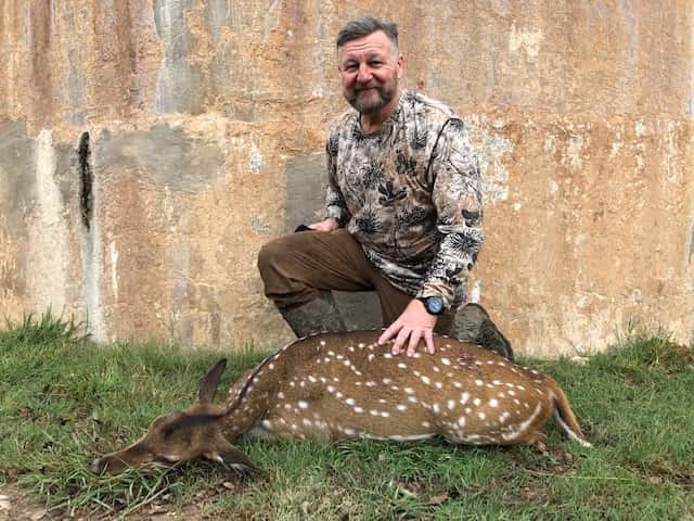 Hunter with an Axis deer beside a round tank