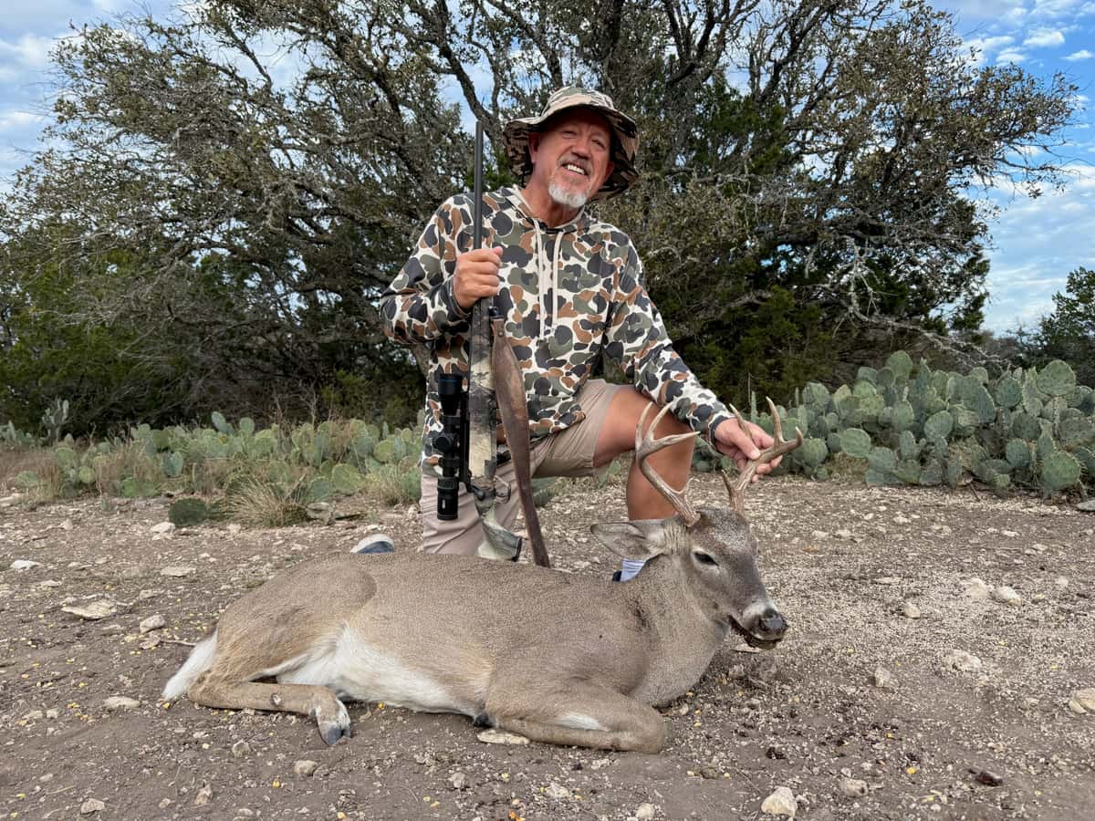Hunter holding a whitetail buck's antlers on rocky ground