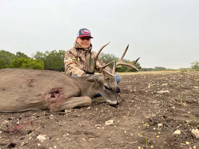 Hunter behind a whitetail buck on bare ground