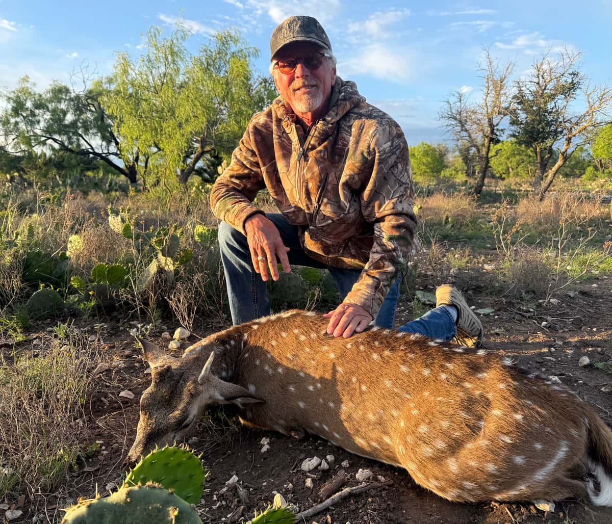 Hunter kneeling beside an Axis buck in evening sunlight