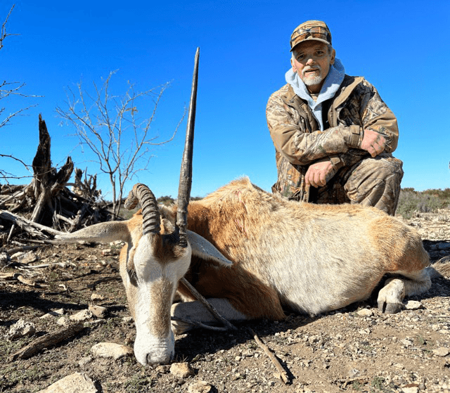 Hunter with an oryx on rocky ground beneath a blue sky