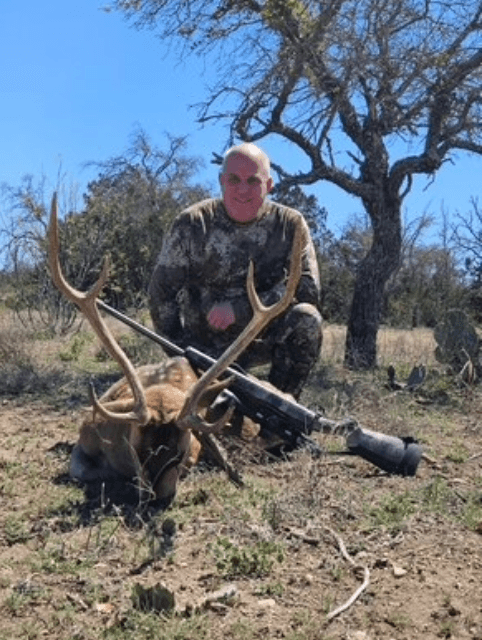 Hunter with an Axis buck beneath a leafless tree