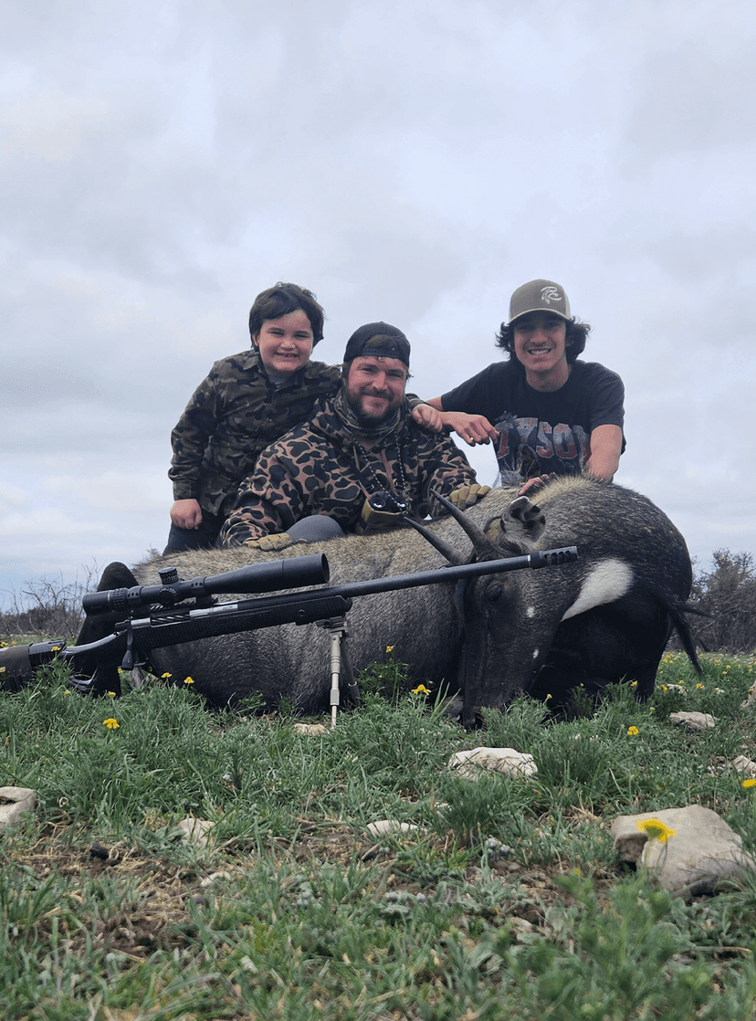Three hunters with a harvested hog in grass
