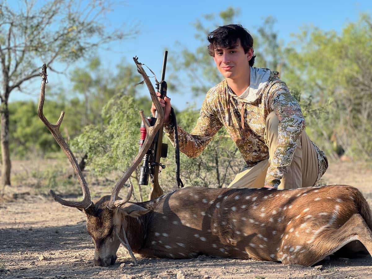 Hunter holding a rifle beside an Axis buck