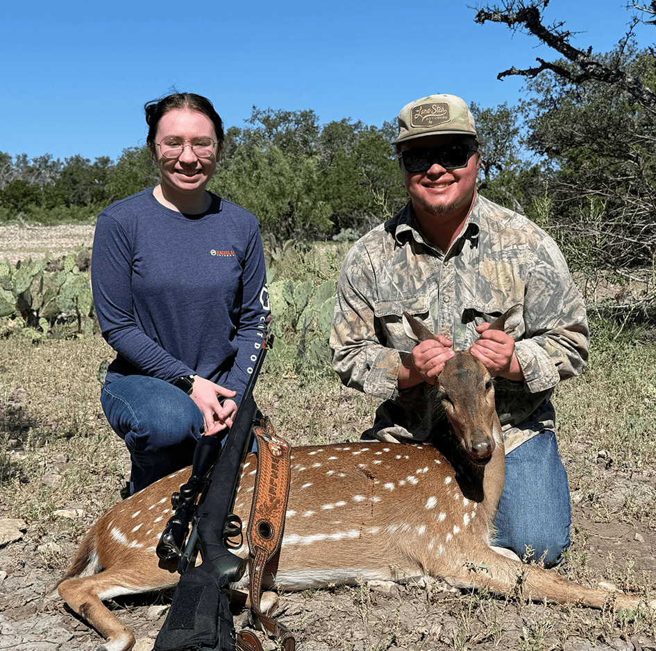 Two hunters with an Axis deer in a sunny clearing