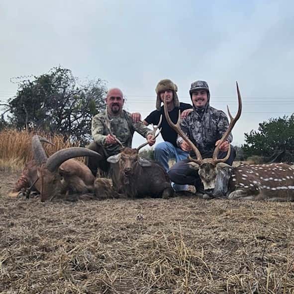 Three hunters with harvested animals in a grassy clearing
