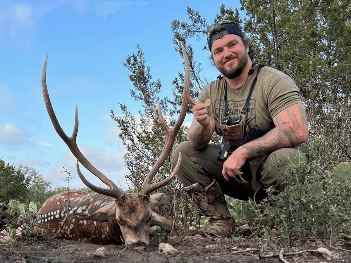 Hunter with an Axis buck in a sunny clearing