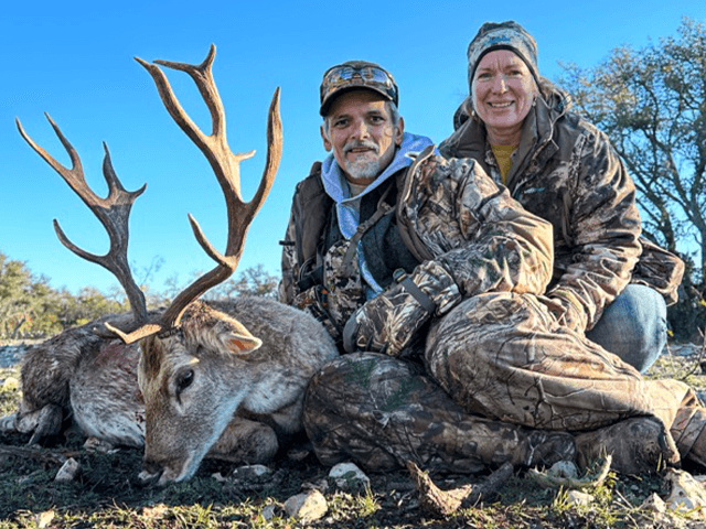 Two hunters seated with a whitetail buck