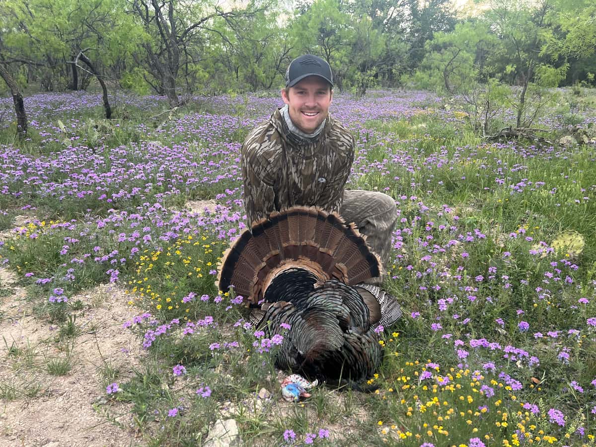 Hunter with a turkey in a field of purple wildflowers