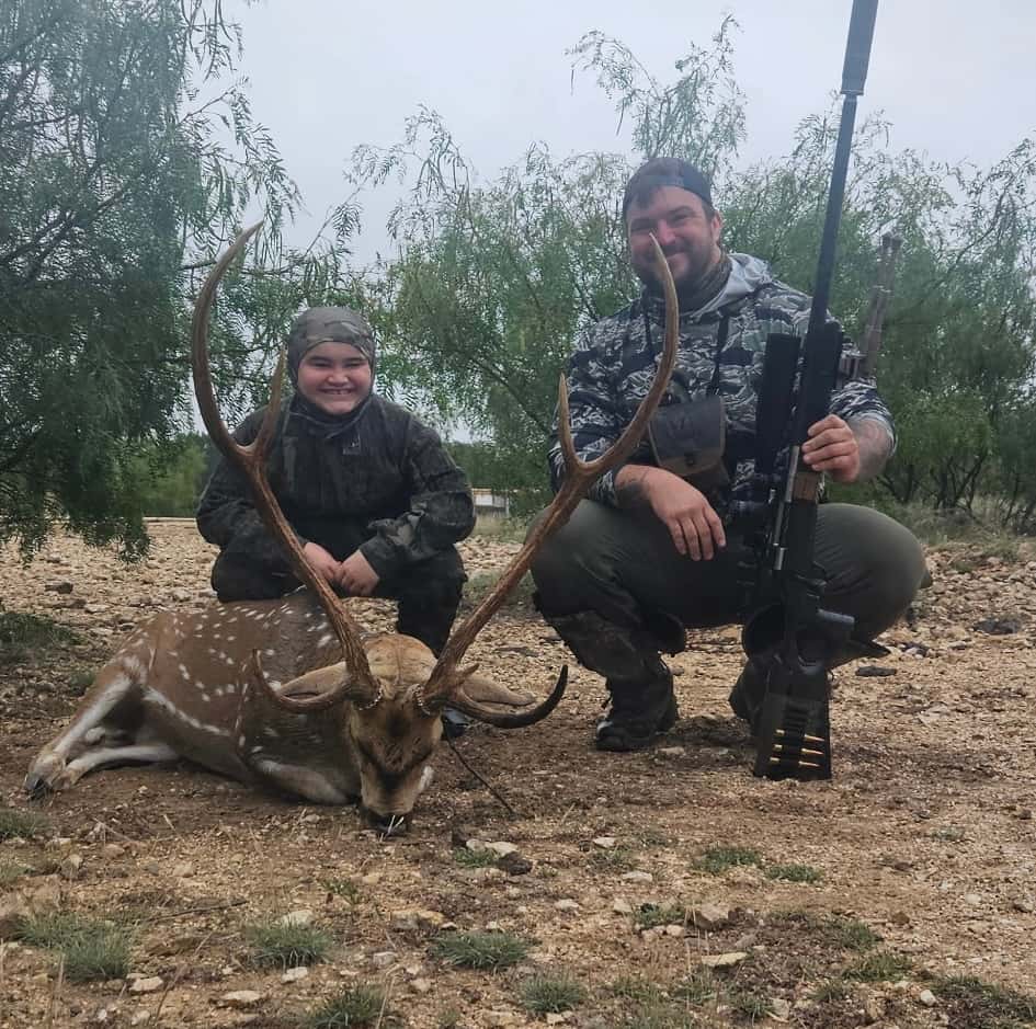 Two hunters with an Axis buck on rocky ground