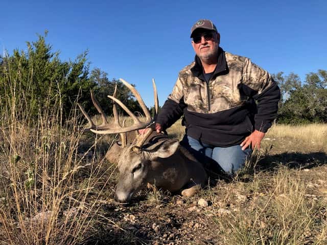 Hunter with a whitetail buck beside a cedar tree