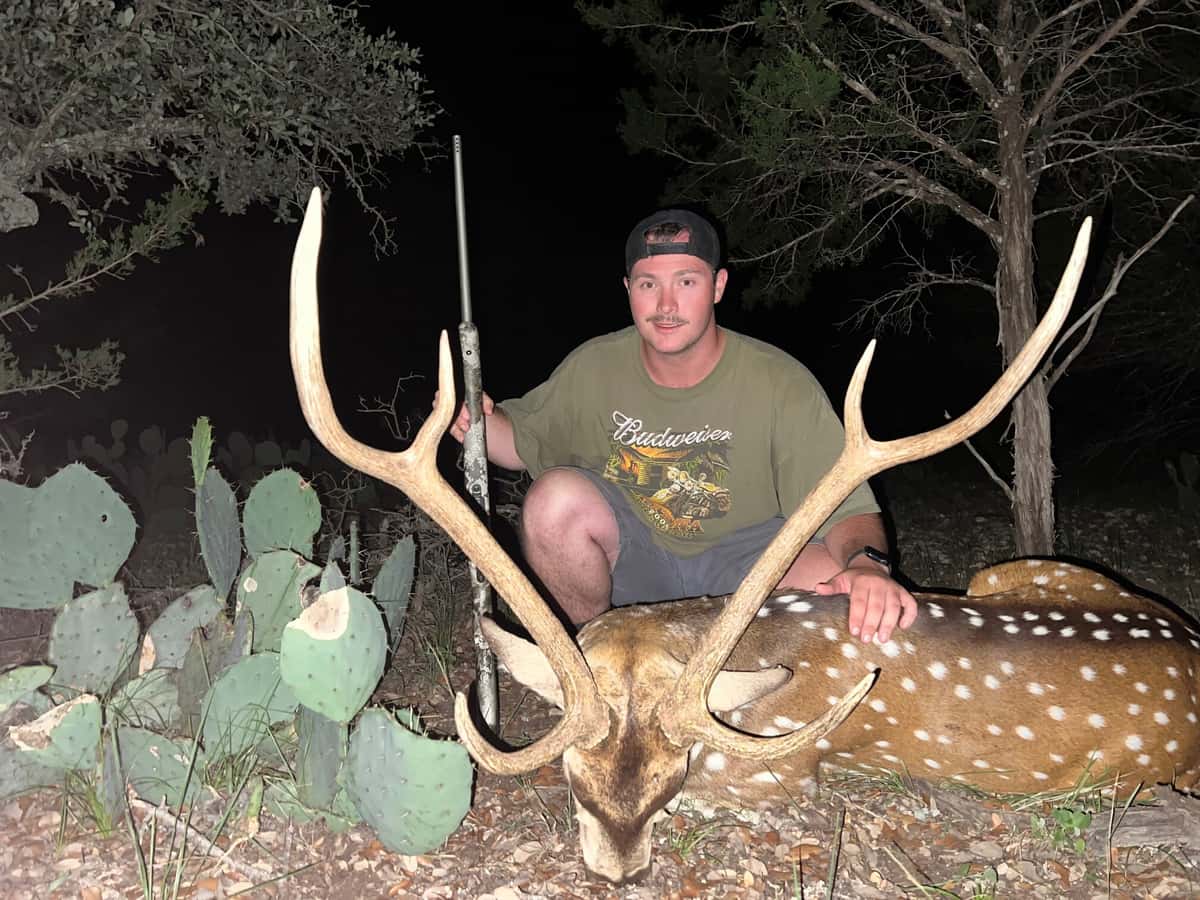 Hunter with an Axis buck beside cactus at night