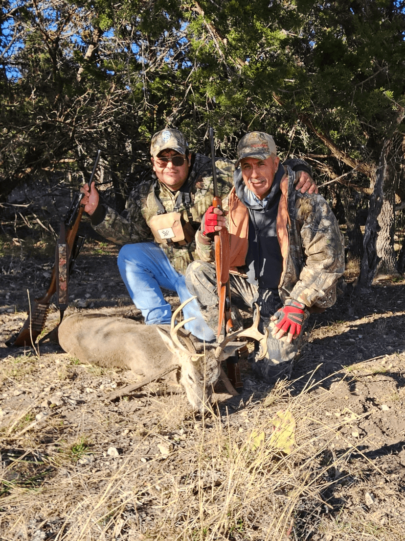 Two hunters kneeling with a whitetail buck beneath a tree