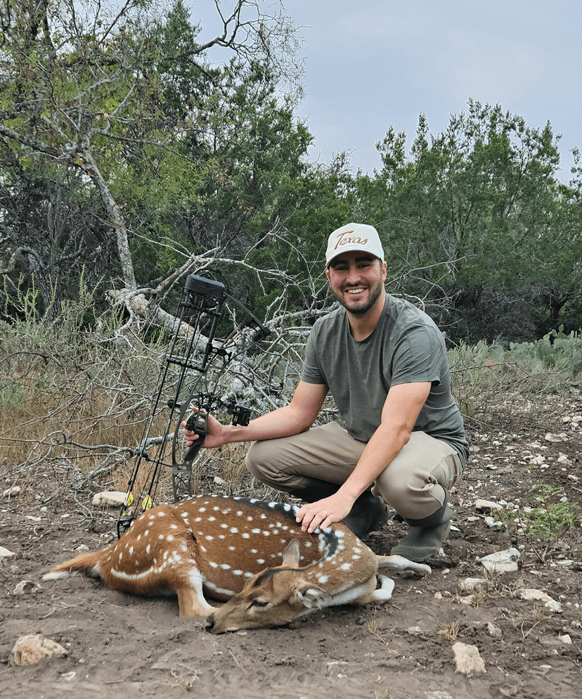Bow hunter with an Axis deer beside trees