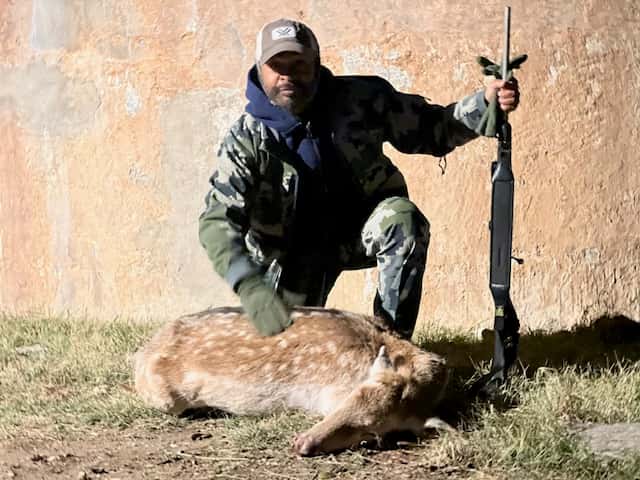 Hunter holding a rifle beside an Axis deer and round tank
