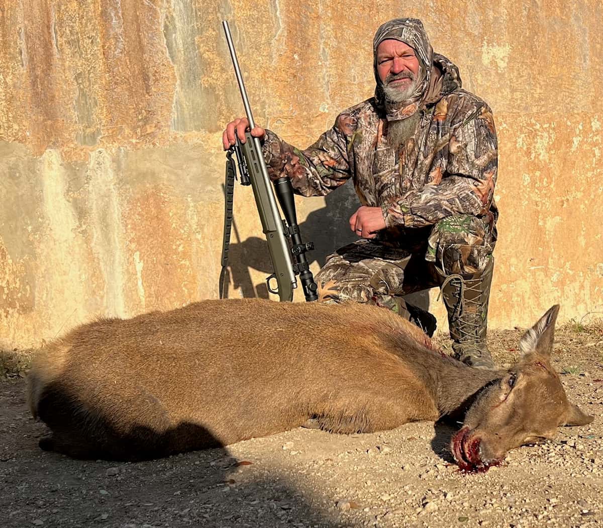 Hunter with a rifle and harvested hog beside a round tank