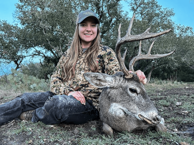 Hunter holding a whitetail buck's antlers in a clearing