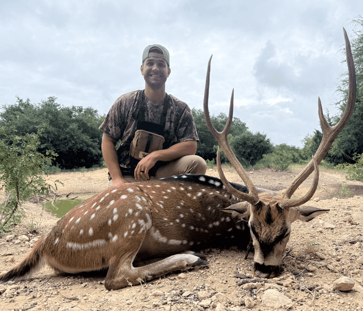 Hunter with an Axis buck in a rocky clearing