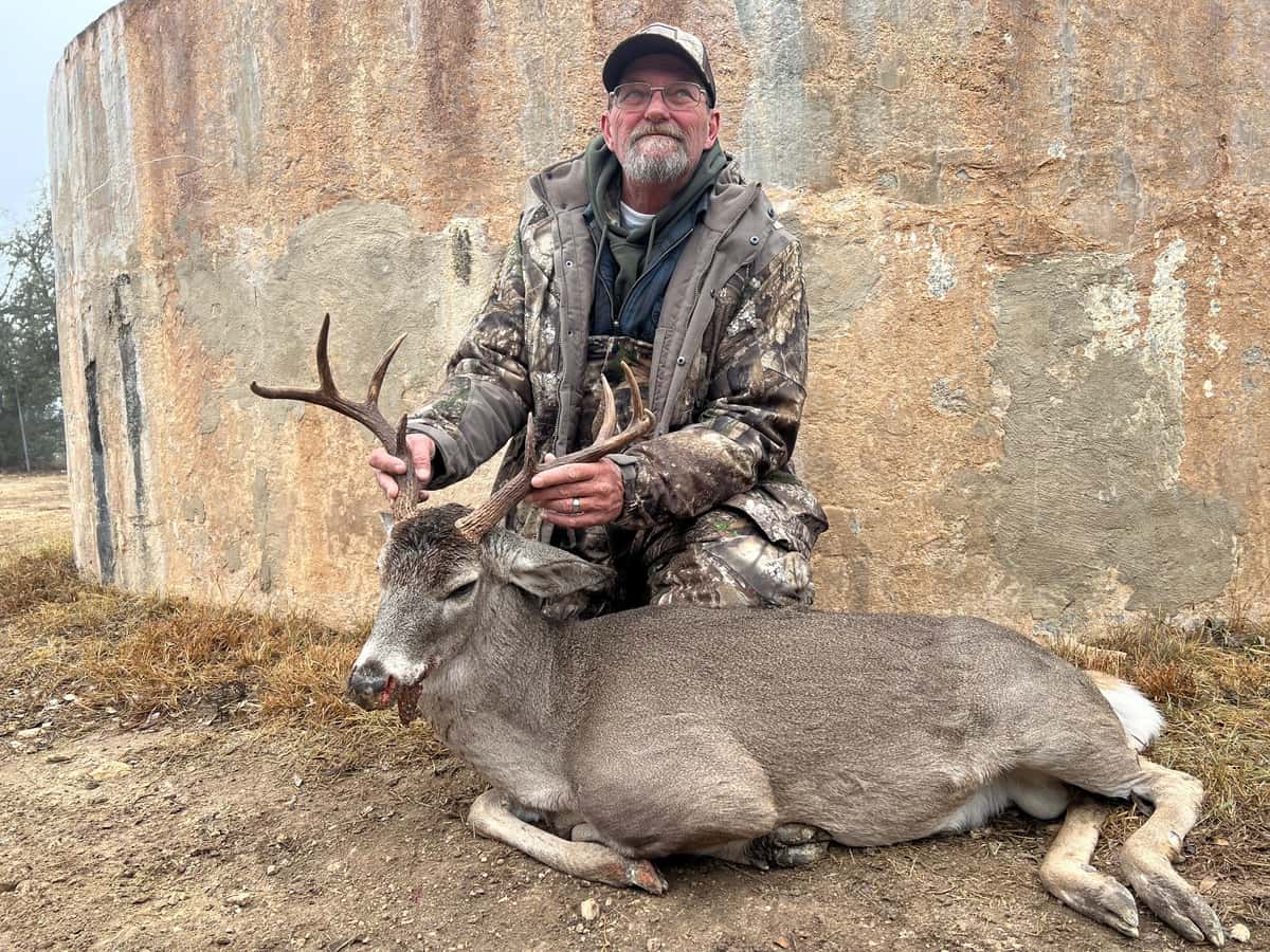 Hunter with a whitetail buck beside a round tank