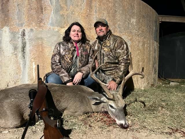 Two hunters with a whitetail buck beside a round tank