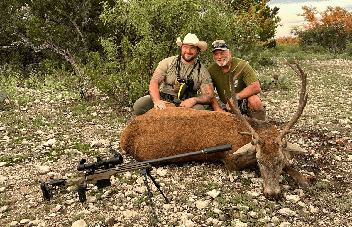 Two hunters with a red stag and rifle on rocky ground