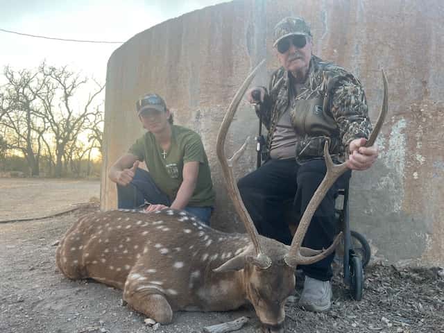 Two hunters with an Axis buck beside a round tank