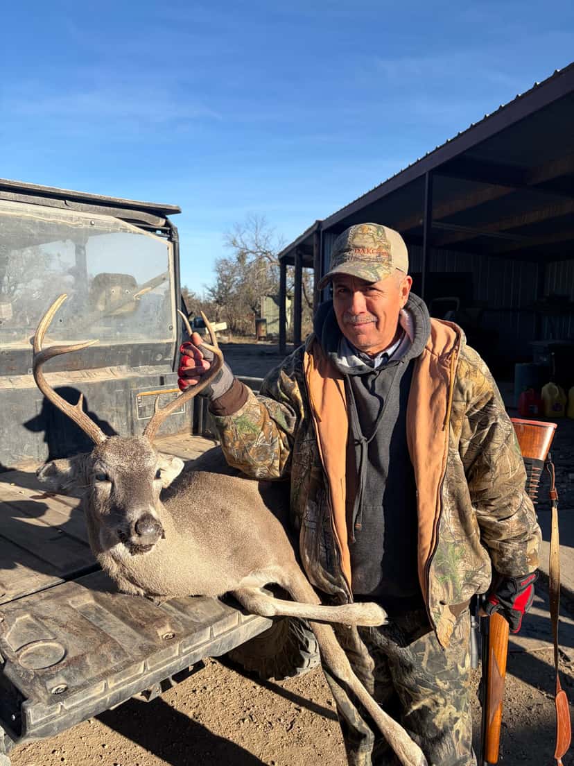 Hunter holding a whitetail buck beside a ranch vehicle