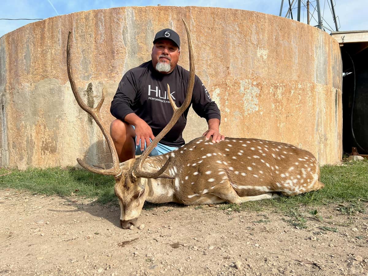 Hunter with an Axis buck beside a round tank