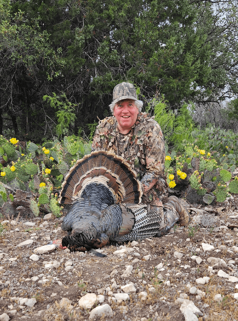 Hunter displaying a turkey beside cactus and wildflowers