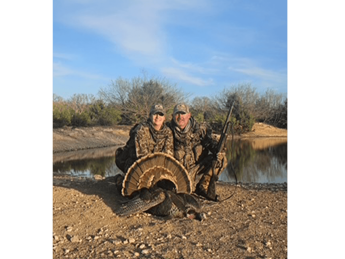 Two hunters with a turkey beside a pond