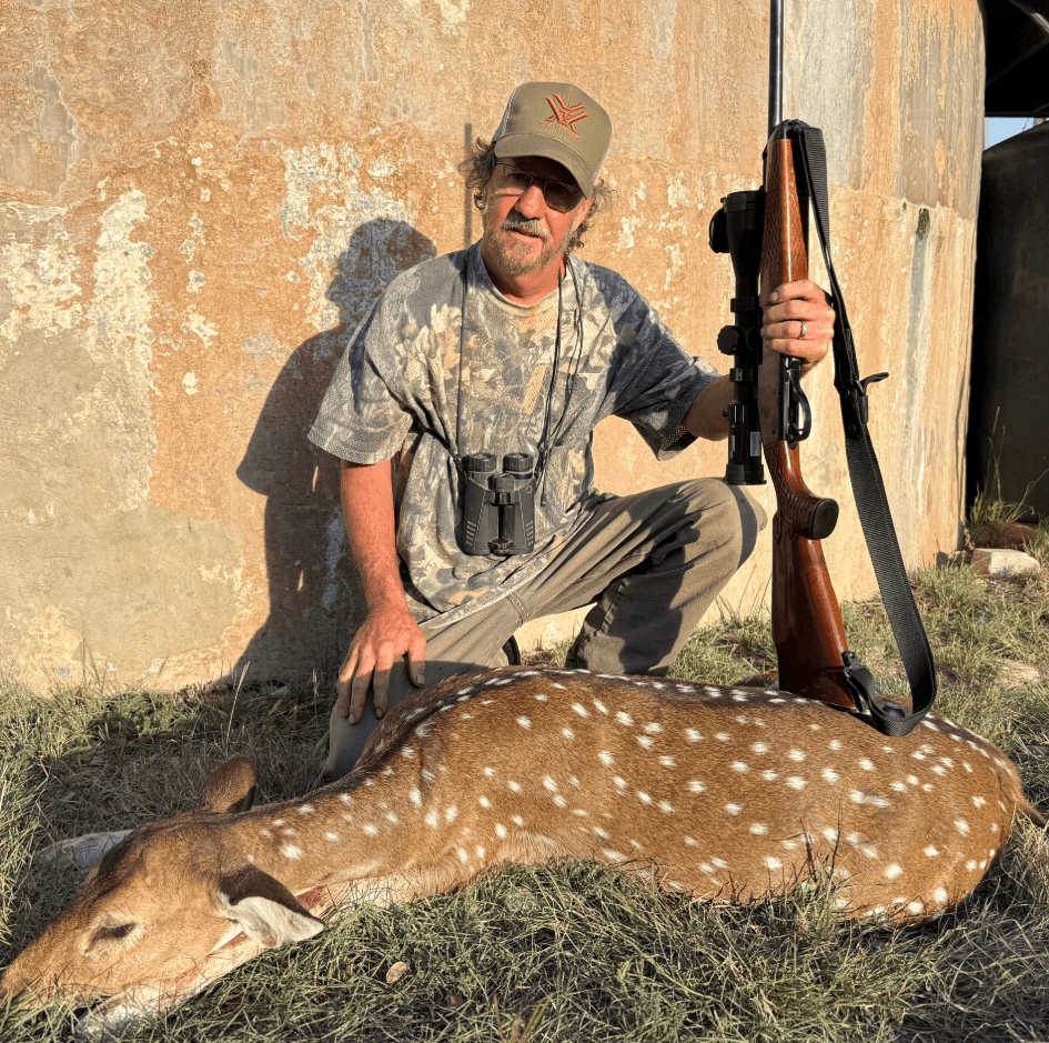 Hunter with an Axis deer and rifle beside a round tank