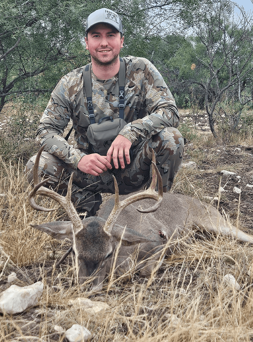 Hunter kneeling with a whitetail buck in dry grass