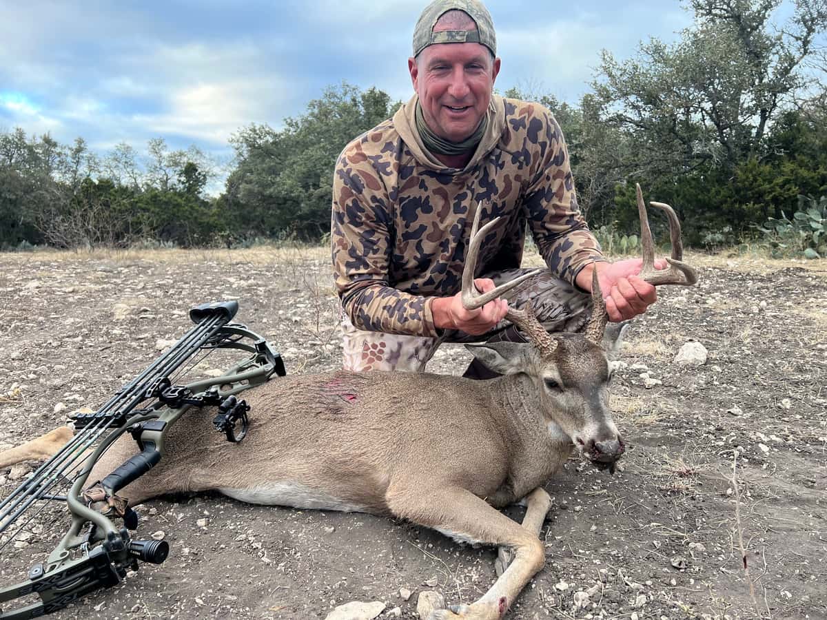 Bow hunter with a whitetail buck on rocky ground