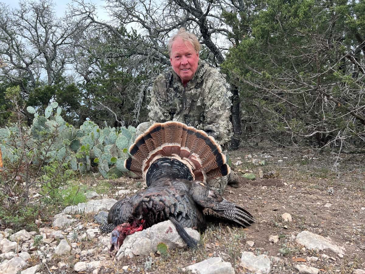 Hunter with a turkey beside prickly pear cactus