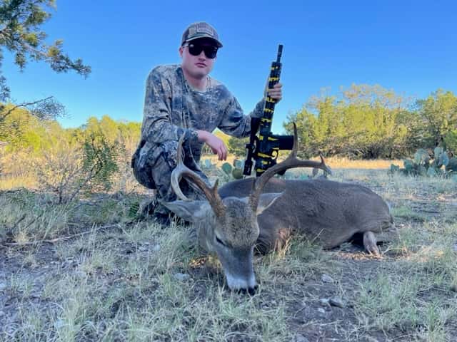 Hunter with a whitetail buck in sunlit grass