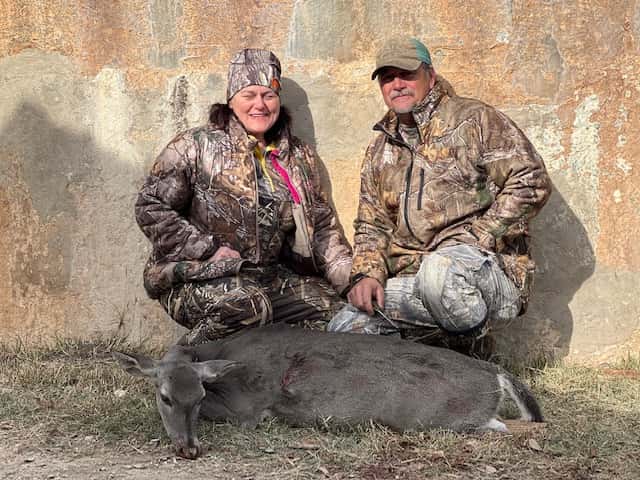 Two hunters with a whitetail buck in front of a tank