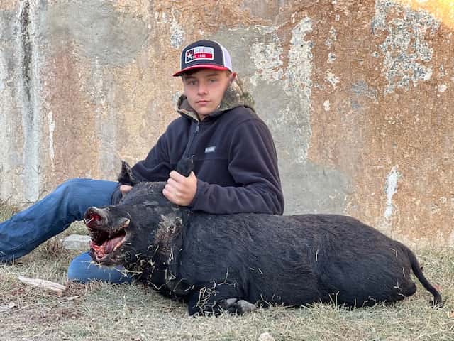 Hunter seated with a black hog beside a round tank