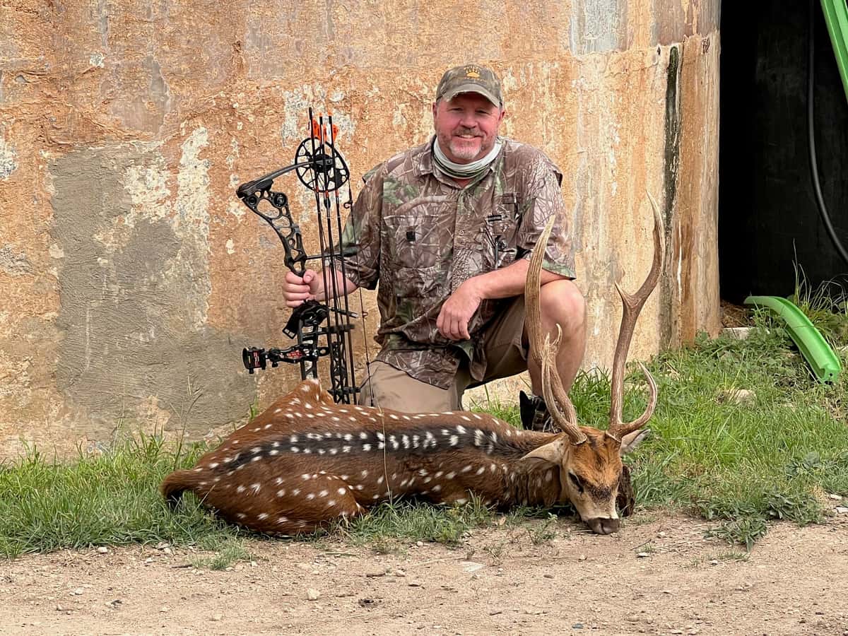 Bow hunter with an Axis buck in front of a round tank