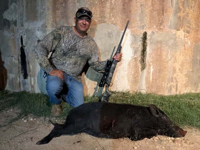 Hunter with a hog and rifle beside a round tank