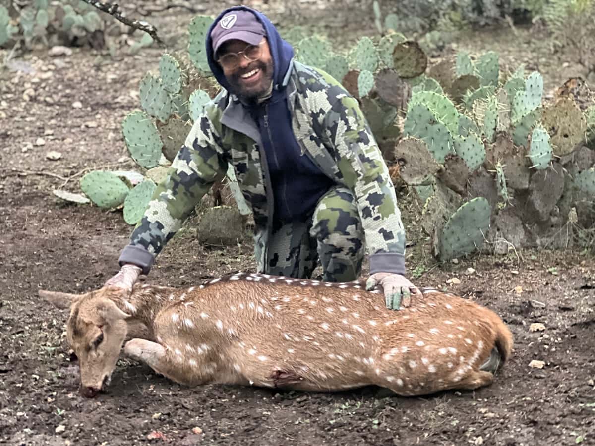 Hunter with an Axis deer beside prickly pear cactus