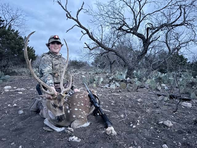 Hunter with an Axis buck beneath leafless trees