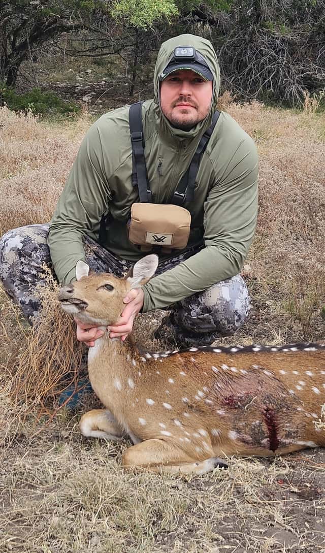 Hunter holding an Axis doe in a grassy clearing