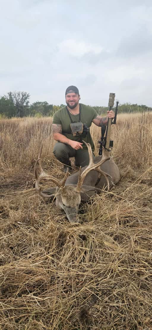 Hunter with a whitetail buck in tall dry grass