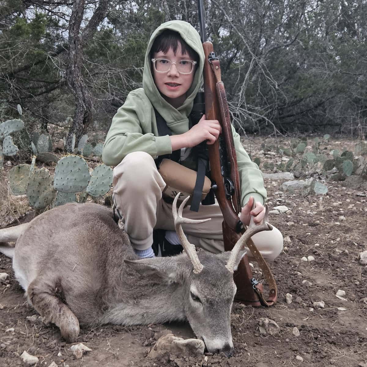 Hunter holding a rifle beside a whitetail buck
